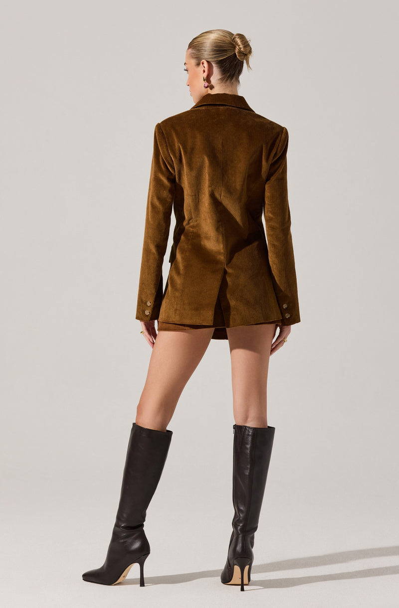 A woman is wearing a brown velvet blazer with long sleeves that have three buttons on each cuff. She is also wearing tall black leather high-heeled boots that reach just below her knees.