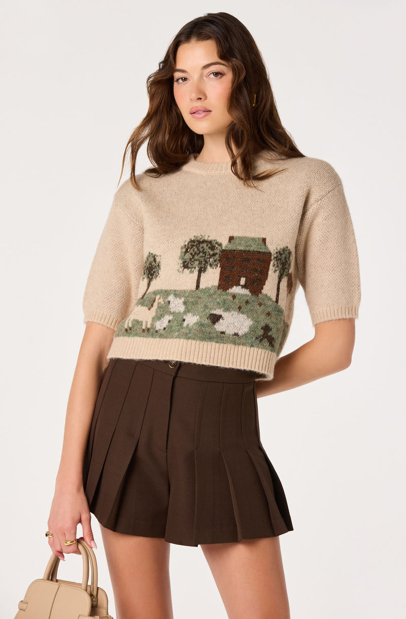 Beige knit sweater with a farm scene and trees, paired with dark brown pleated shorts.
