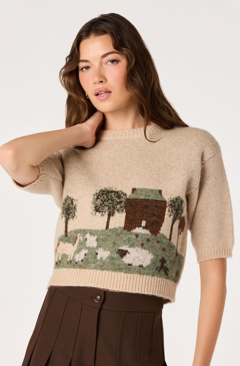 Beige knit sweater with a landscape scene featuring trees, a house, sheep, and a pond.
