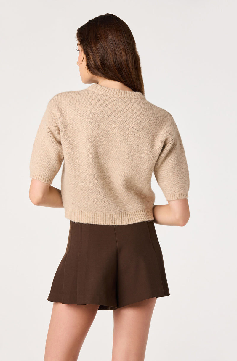 Woman wearing a beige knitted short-sleeve sweater and high-waisted brown shorts.