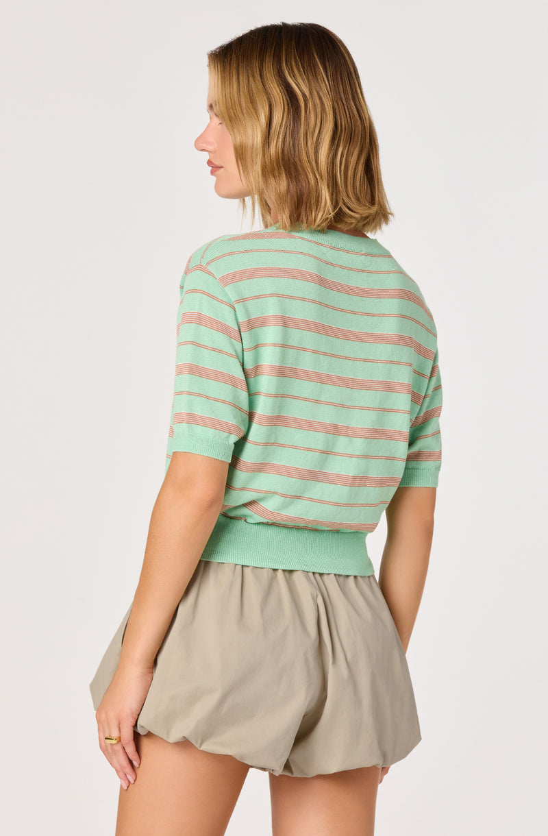 Woman in pastel green and pink striped short-sleeve sweater with beige shorts.