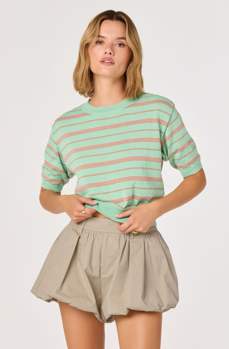 Woman wearing a mint green and pink striped short-sleeve knit top with beige high-waisted shorts.