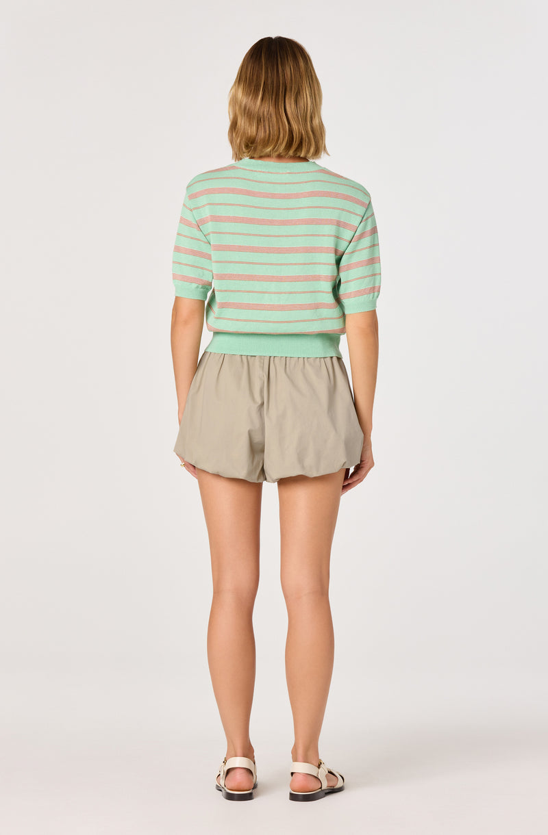 Woman wearing a green and pink striped short-sleeved sweater and beige shorts.