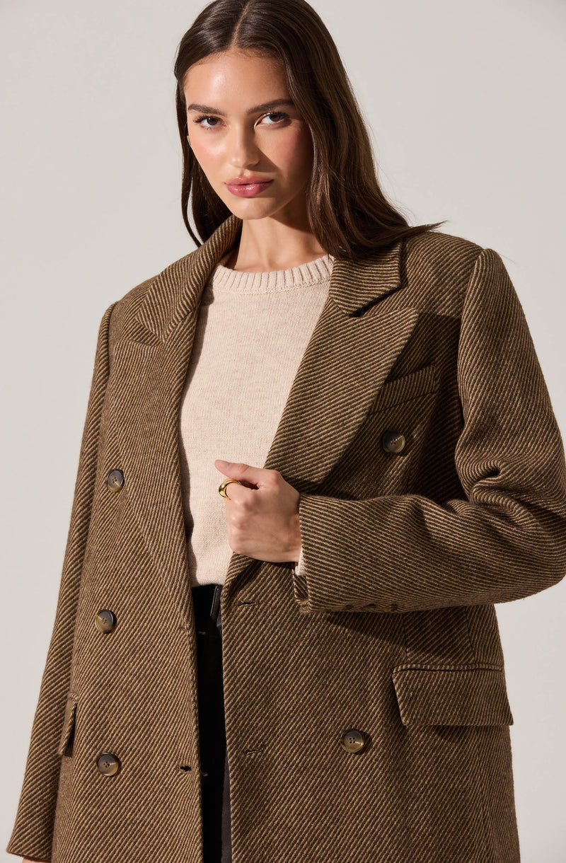 A woman is wearing a brown double-breasted herringbone plaid coat with wide lapels and large buttons. Underneath, she has on a beige knit sweater.