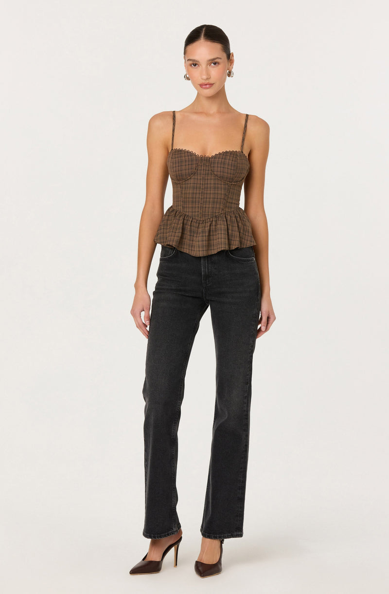 A woman is wearing a fitted, brown checkered top with thin spaghetti straps and a ruffled hem. She pairs it with high-waisted, dark-wash jeans and pointed-toe high heels.