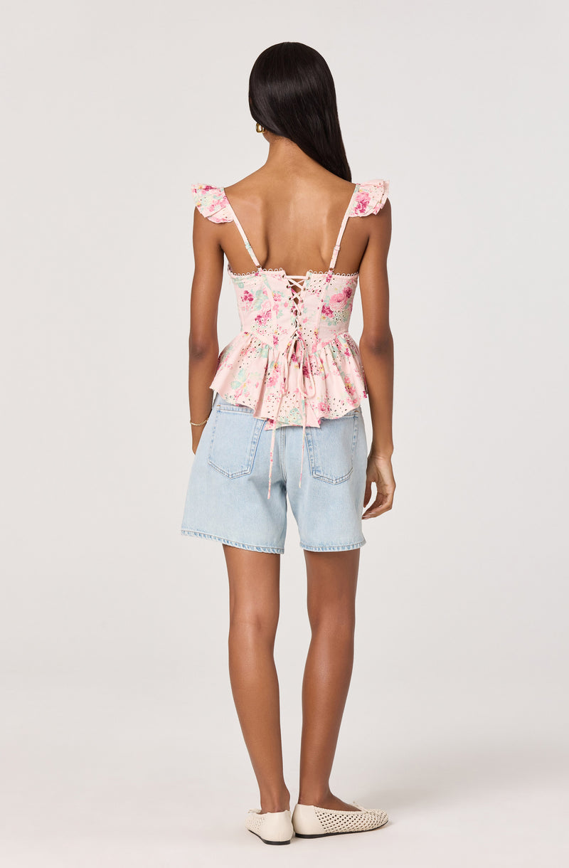 Woman wears a pink floral ruffled top with lace-up back and light blue denim shorts.