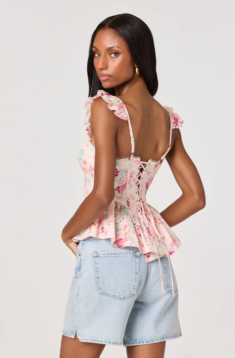 Woman in pink floral ruffled top with lace-up back and light-wash denim shorts.