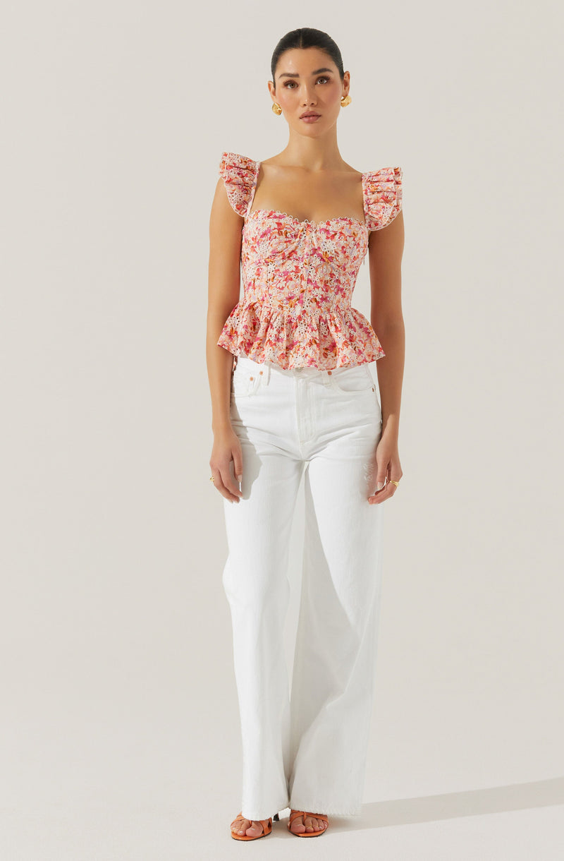 A woman is wearing a pink floral blouse with ruffled cap sleeves, a square neckline, and a peplum waist. She is also wearing high-waisted, wide-leg white pants and open-toe sandals.