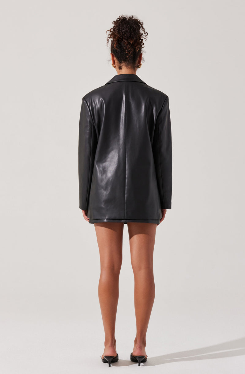 The person is wearing a black leather blazer with a tailored fit. The blazer is long, extending to the upper thighs. They are also wearing black pointed-toe high heels.