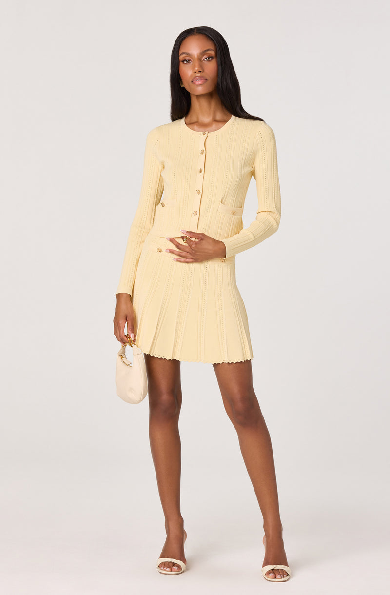 Cream yellow knit cardigan and skirt set, with gold buttons, paired with white high heels.