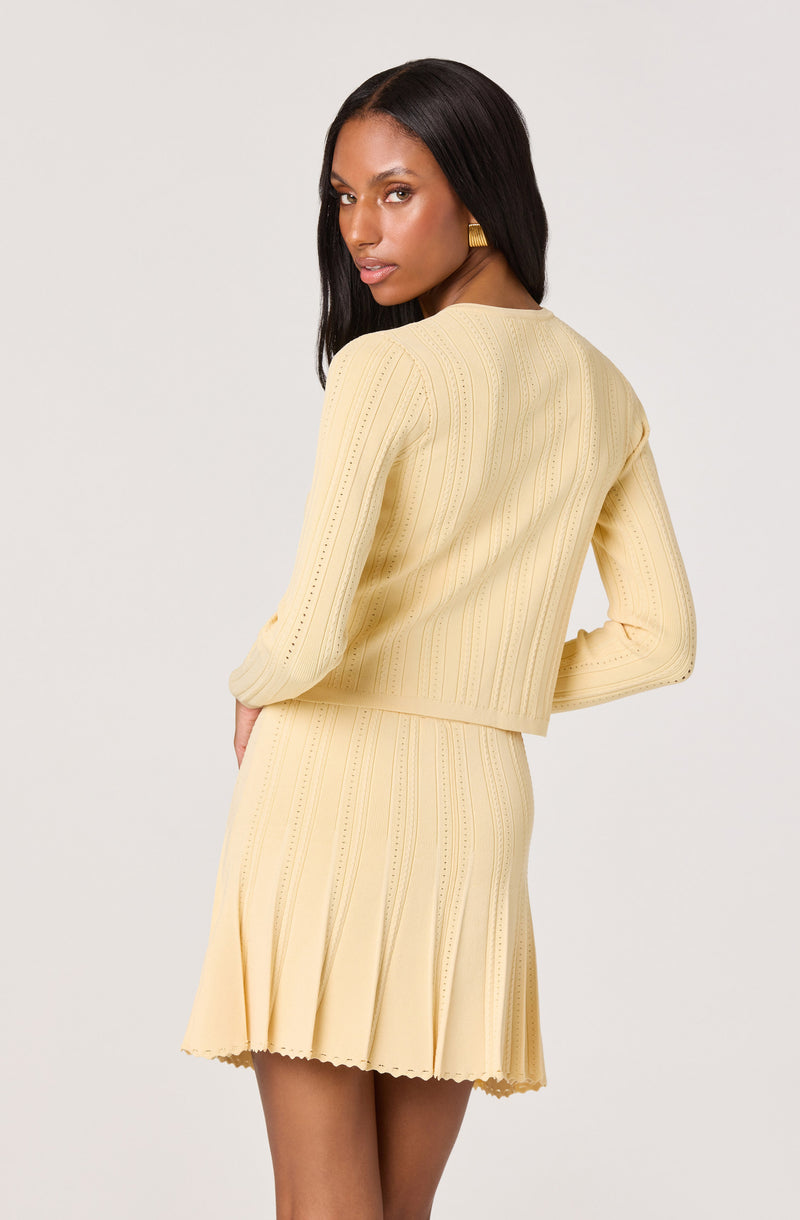 Woman in a light yellow, ribbed sweater and matching pleated skirt.