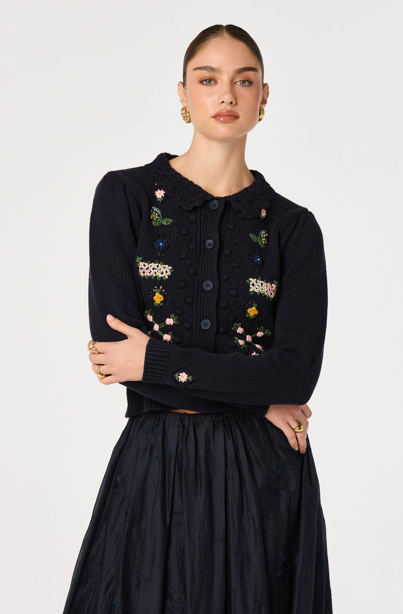 Women wearing a dark knit cardigan with colorful floral embroidery and a scalloped collar.