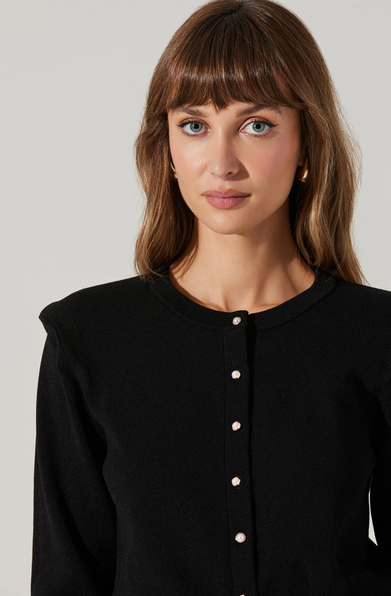A woman is wearing a black cardigan with a round neckline. The cardigan has a row of pearl-like buttons down the front.