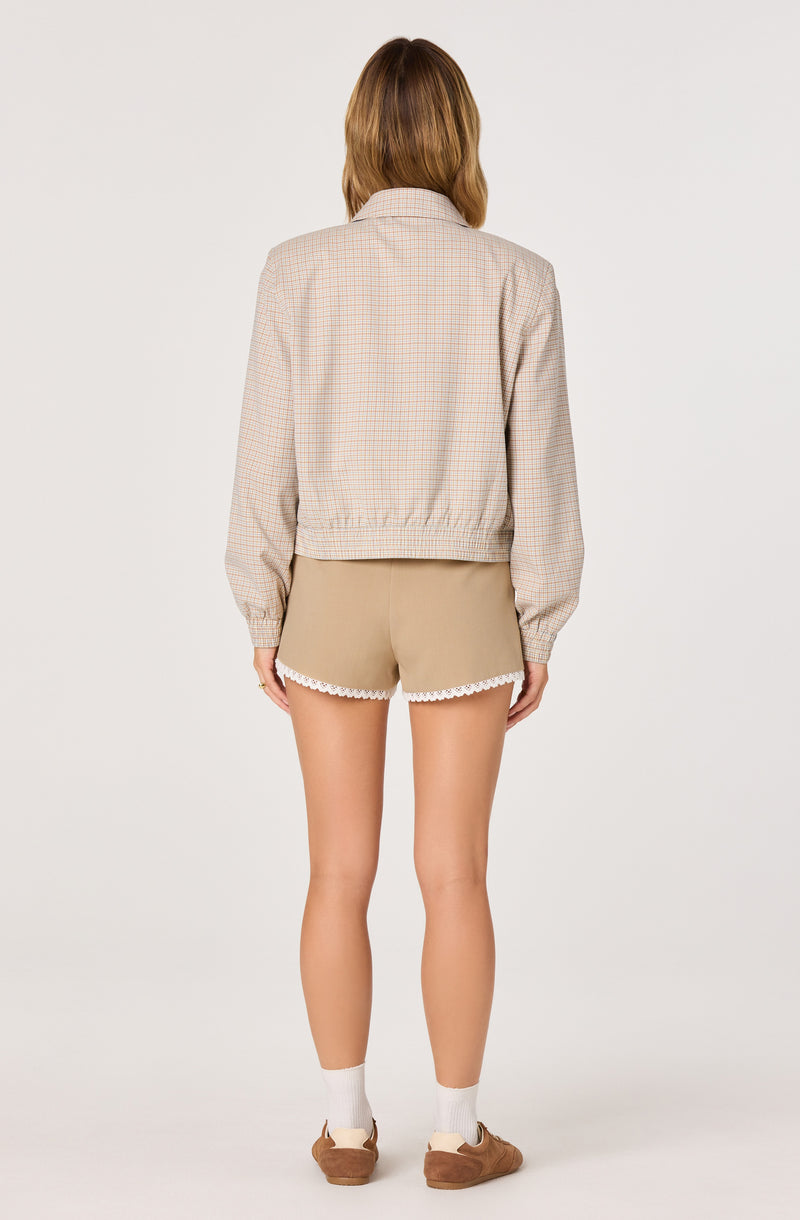 Girl wearing beige shorts with white lace trim, a light checkered jacket, white socks, and brown shoes.
