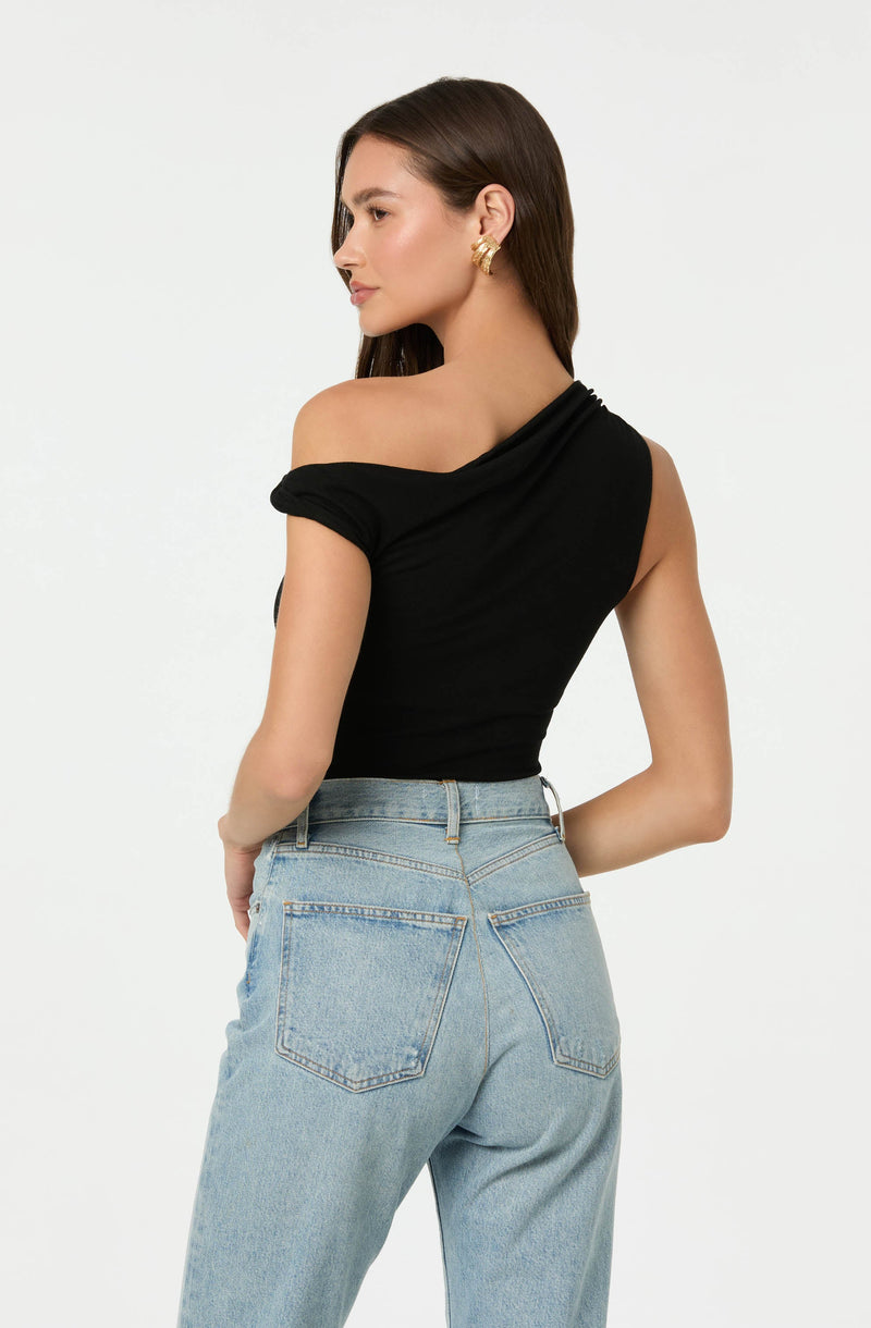 A woman is wearing an off-the-shoulder black top with a draped neckline and short sleeves that are rolled up. She has paired it with high-waisted light blue jeans that have a classic five-pocket design. She accessorized with gold hoop earrings.