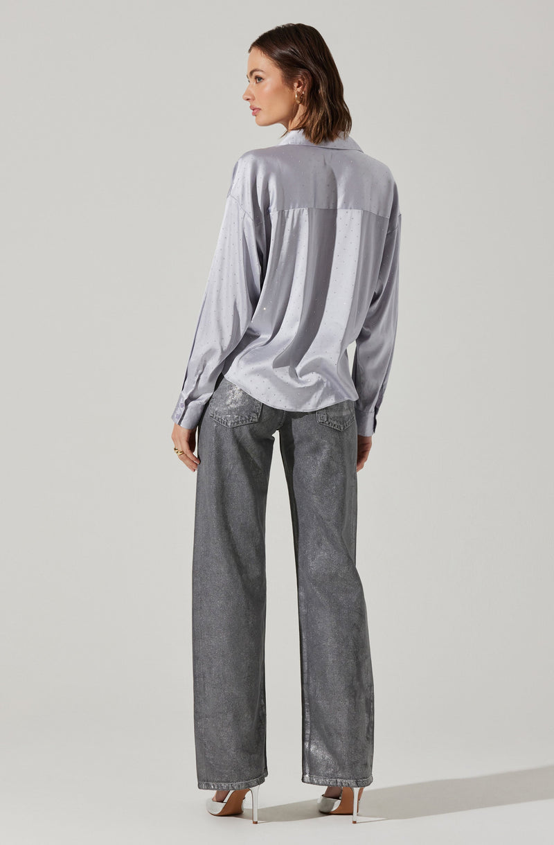 A woman is wearing a light gray, long-sleeved, satin shirt with a slightly loose fit, featuring a yoke detail across the back. She pairs it with high-waisted, wide-leg gray jeans with a textured, washed appearance. She completes the look with beige high-heeled shoes.