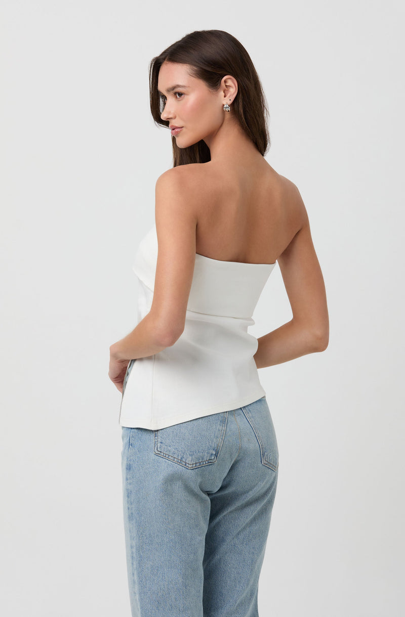 A woman is wearing a strapless white top that is fitted at the waist and light blue high-waisted jeans with a relaxed fit.
