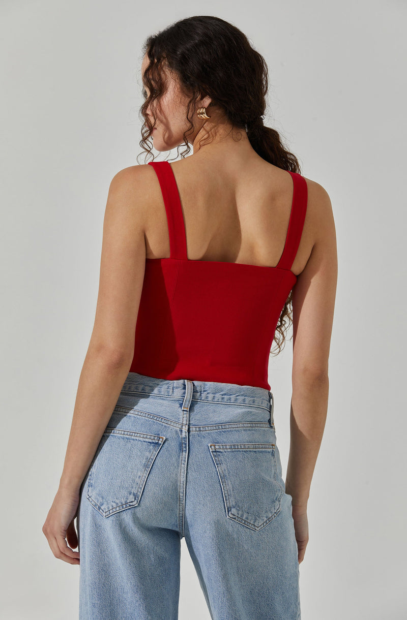 A woman is wearing a fitted red tank top with wide shoulder straps and a square neckline, paired with light blue high-waisted jeans that have a relaxed fit and classic five-pocket styling.