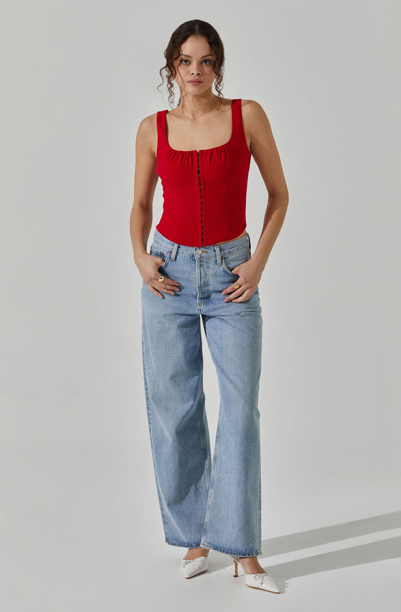 A woman wearing a fitted red sleeveless top with a square neckline and button detail down the front, paired with high-waisted light blue wide-leg jeans and white heels.