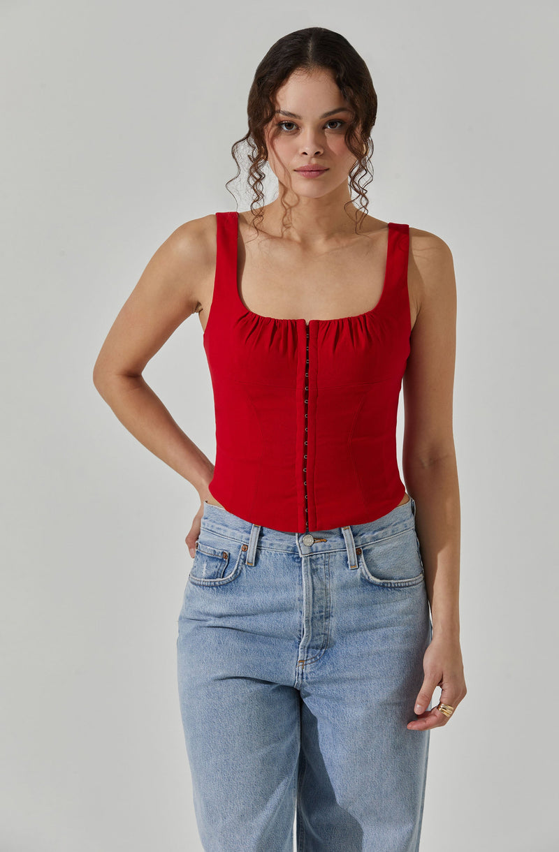 A woman is wearing a sleeveless red top with a square neckline and gathered fabric detail at the front, paired with light blue high-waisted jeans.