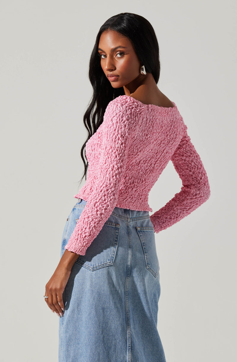 A woman is wearing a light pink, textured, long-sleeve top with a boat neckline and a high-waisted, light blue denim skirt. The top has a soft, fuzzy appearance, and the skirt features classic denim details with visible stitching and back pockets.
