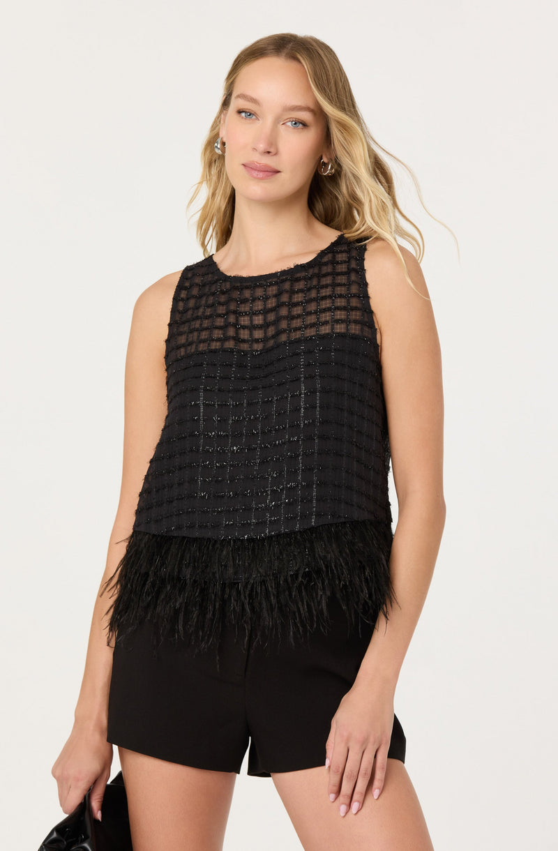 A woman is wearing a sleeveless black top made of a checkered, sheer fabric with a dotted pattern. The top features a feathered trim at the hem. She pairs it with black shorts.
