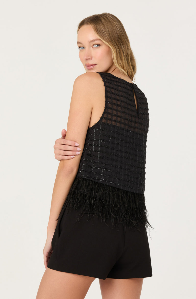 A woman is wearing a sleeveless black top with a textured, checkered pattern and a small keyhole opening at the back, paired with black shorts. The top features a feathered hemline at the bottom.