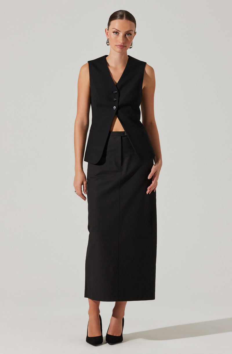 A woman is wearing a sleeveless black vest with buttons down the front, paired with a high-waisted, full-length black skirt. She is also wearing black high-heeled shoes.