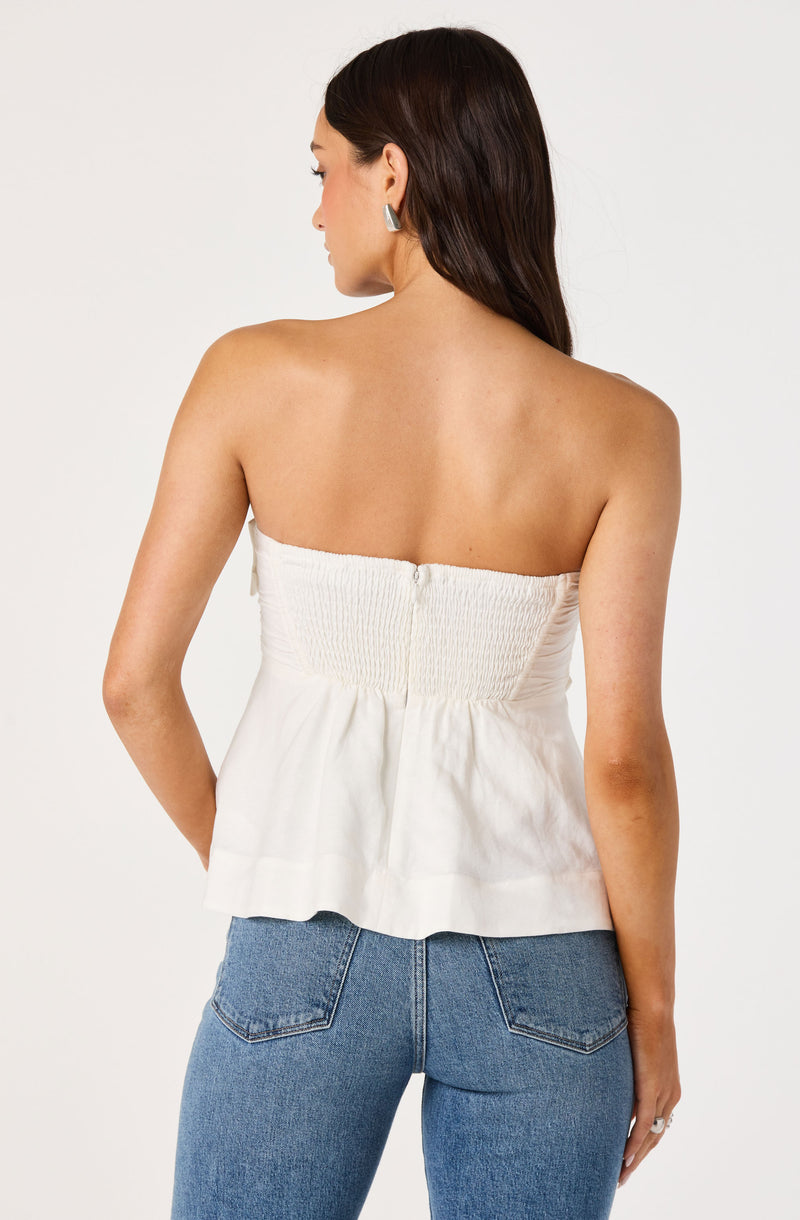 White strapless top with smocked bodice and peplum-style hem, paired with blue jeans.
