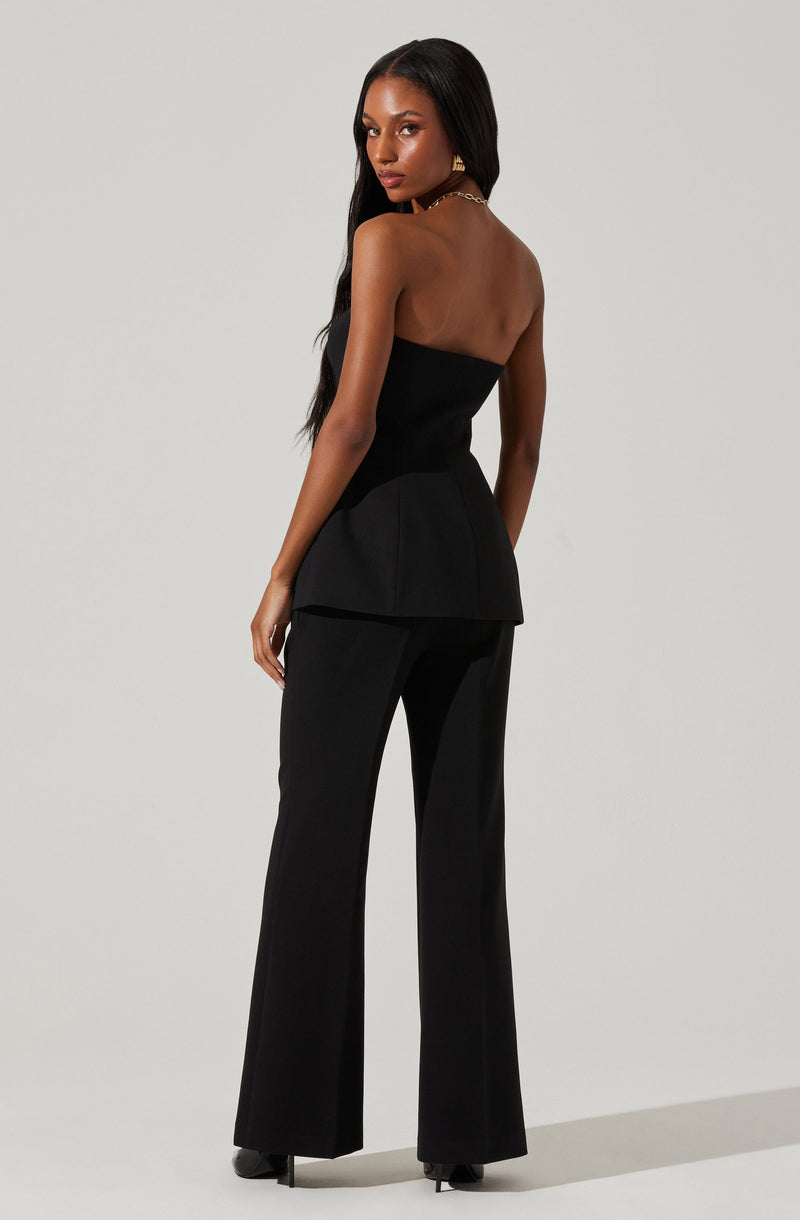 A woman is wearing a strapless black top with a peplum detail at the waist and matching black wide-leg trousers.
