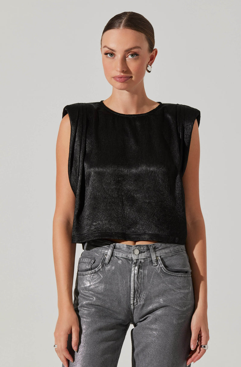 A woman is wearing a sleeveless, black top with padded shoulders and a shiny, textured fabric. She pairs it with high-waisted, gray jeans that have a slightly faded, metallic appearance.