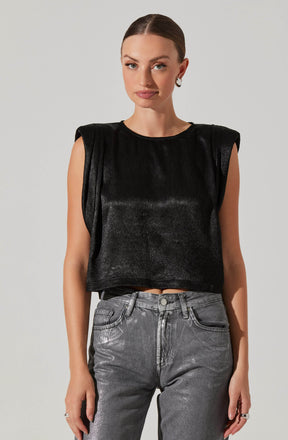 A woman is wearing a sleeveless, black top with padded shoulders and a shiny, textured fabric. She pairs it with high-waisted, gray jeans that have a slightly faded, metallic appearance.