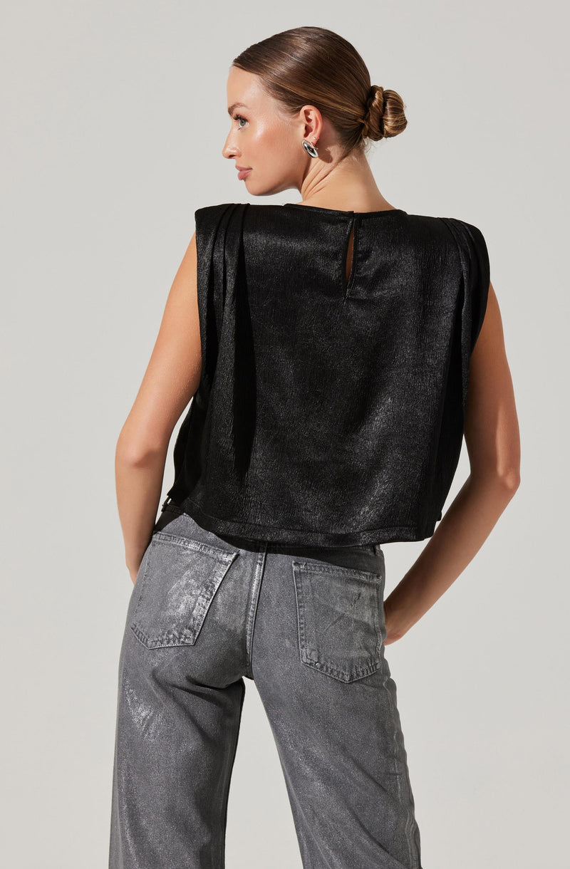 A woman is wearing a sleeveless black top with a shiny, textured fabric and structured shoulder details. The top has a small keyhole opening at the back neckline. She is also dressed in high-waisted gray jeans with a slightly faded wash and visible back pockets.