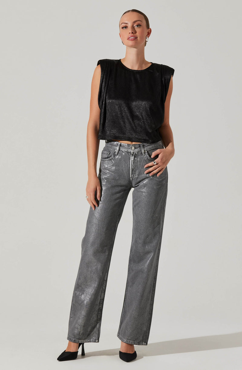 A woman is wearing a sleeveless black top with a shiny, slightly textured fabric. She pairs it with high-waisted, straight-leg jeans in a faded grey color. She completes the outfit with black high-heeled shoes.