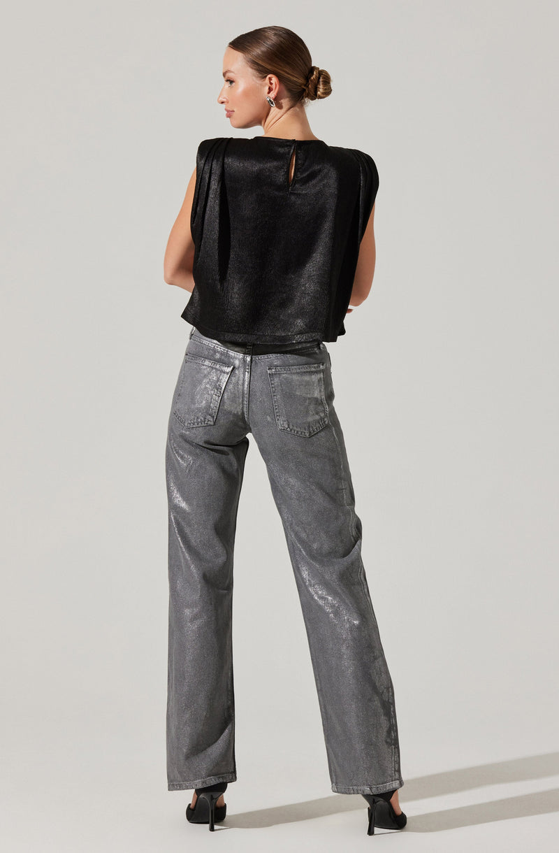 A woman is wearing a sleeveless black top with a shiny, textured fabric and a small keyhole opening at the back. She pairs it with high-waisted, loose-fitting gray jeans that have a faded, slightly distressed look. The outfit is completed with black high-heeled shoes.