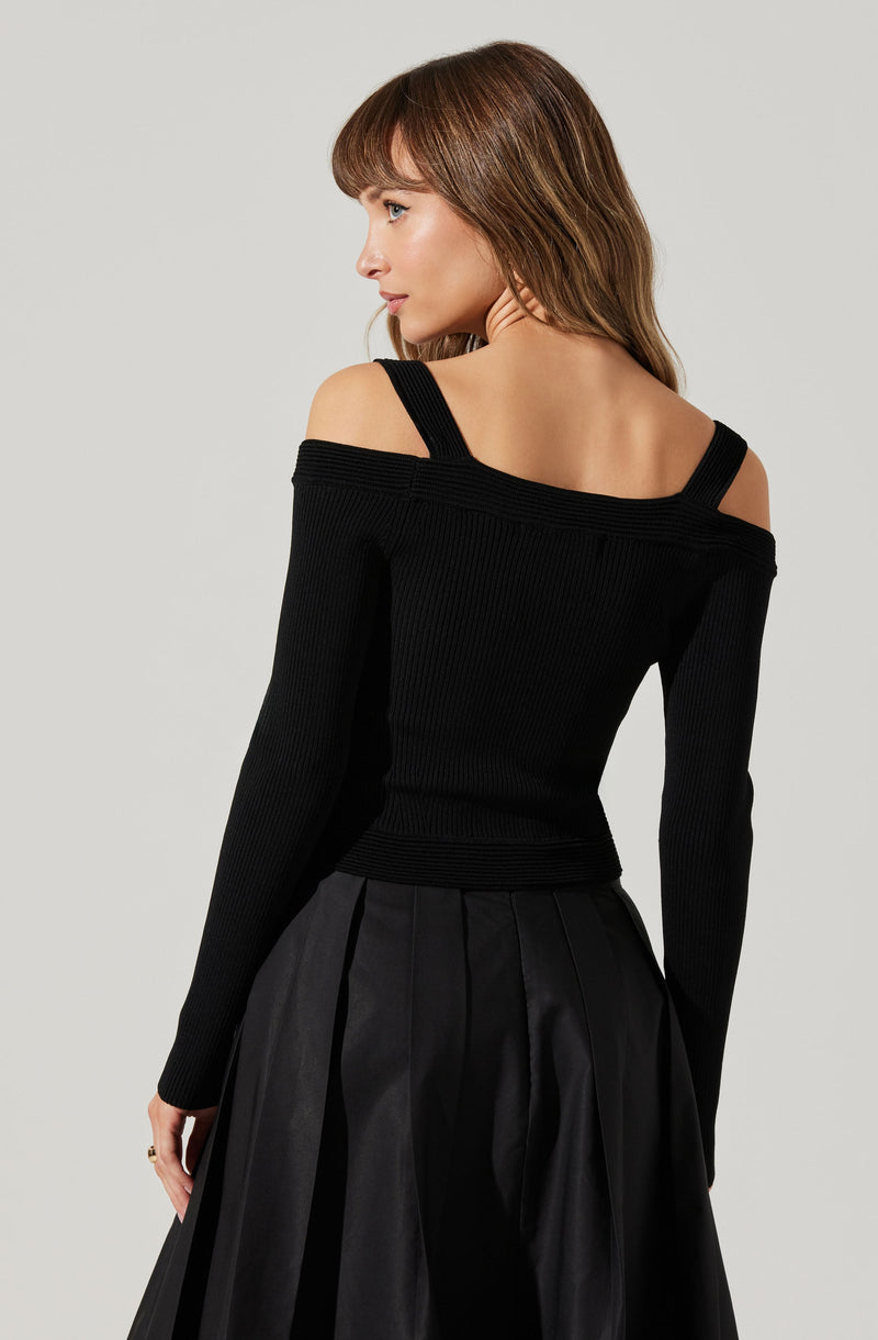 A woman is wearing a black, ribbed, off-the-shoulder sweater with wide straps. She pairs it with a black, pleated, shiny midi skirt.