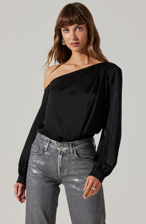 A woman is wearing a one-shoulder black satin blouse with long, billowy sleeves gathered at the wrists, paired with high-waisted, acid-wash gray jeans.