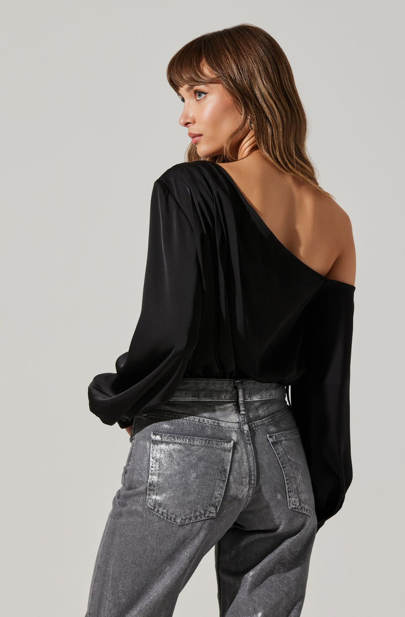 A woman is wearing a black, off-the-shoulder top with long, loose sleeves made of a shiny, satin-like fabric. She is also wearing high-waisted, gray, acid-wash jeans.