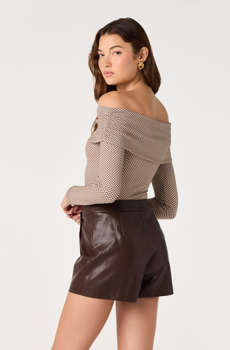 Woman wearing an off-the-shoulder patterned top and high-waisted brown leather shorts.
