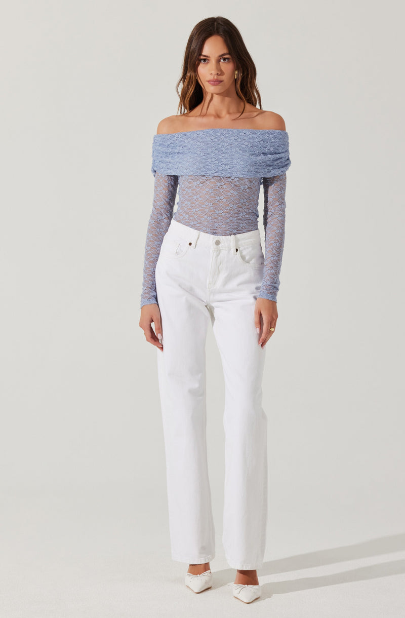 A woman is wearing an off-the-shoulder light blue top that features long, fitted sleeves and a wide, textured band across the shoulders. She pairs it with high-waisted, straight-leg white jeans and white pointed-toe shoes.