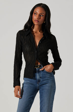 A woman is wearing a black, long-sleeved, button-up cardigan with a textured, ribbed pattern. She pairs it with high-waisted blue denim jeans.
