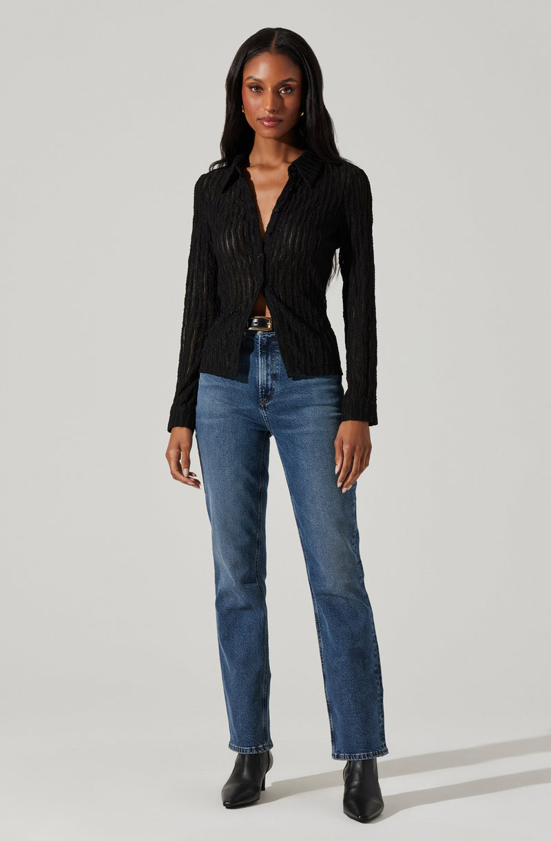 A woman is wearing a black, long-sleeved, textured sweater with a collar and a button-down front. She has paired it with blue high-waisted jeans and black ankle boots.
