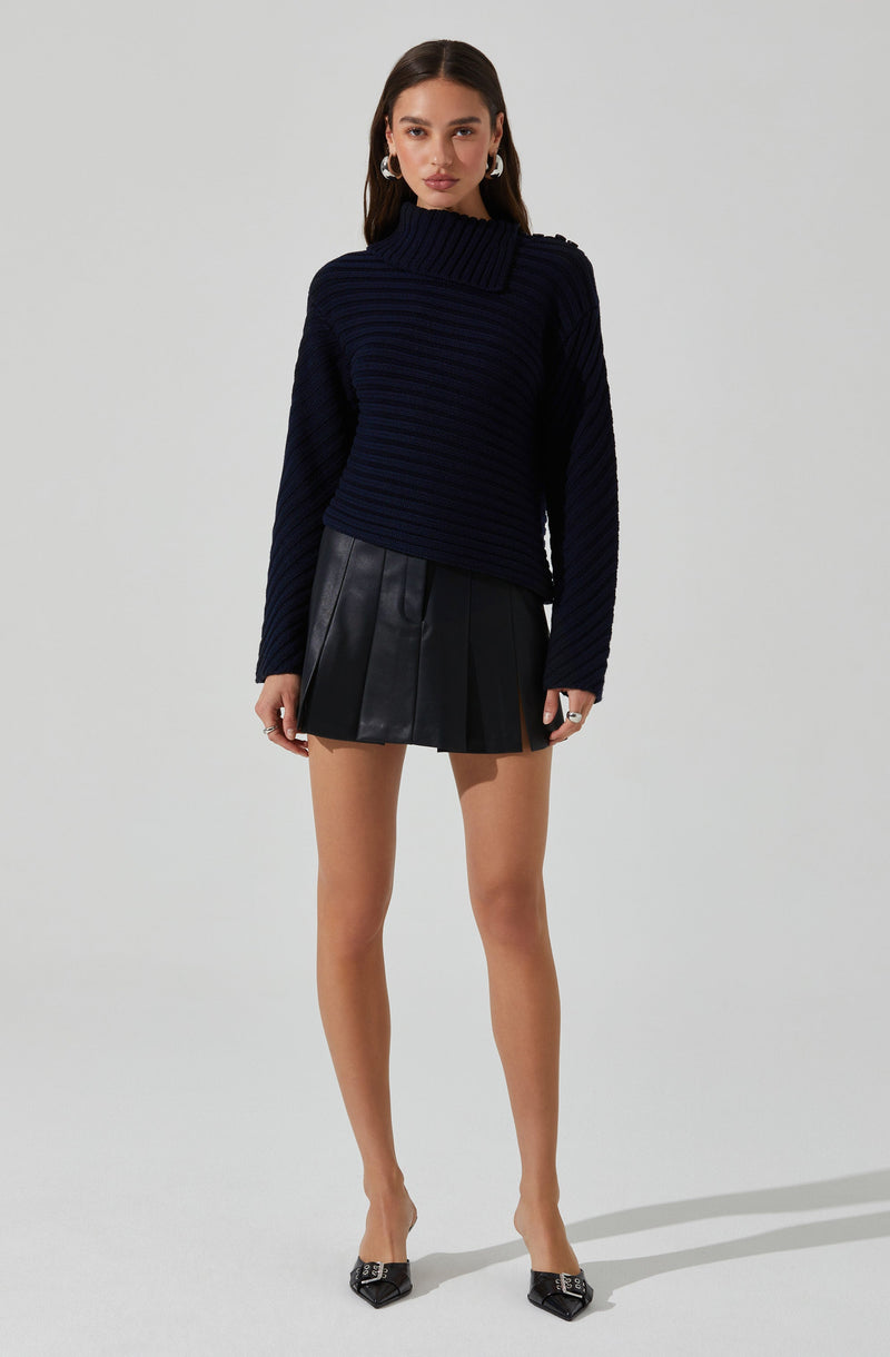 A woman is wearing a dark navy, ribbed, turtleneck sweater with asymmetric shoulder details, paired with a black leather mini skirt featuring pleats. She completes her outfit with black pointed-toe heels with embellishments.