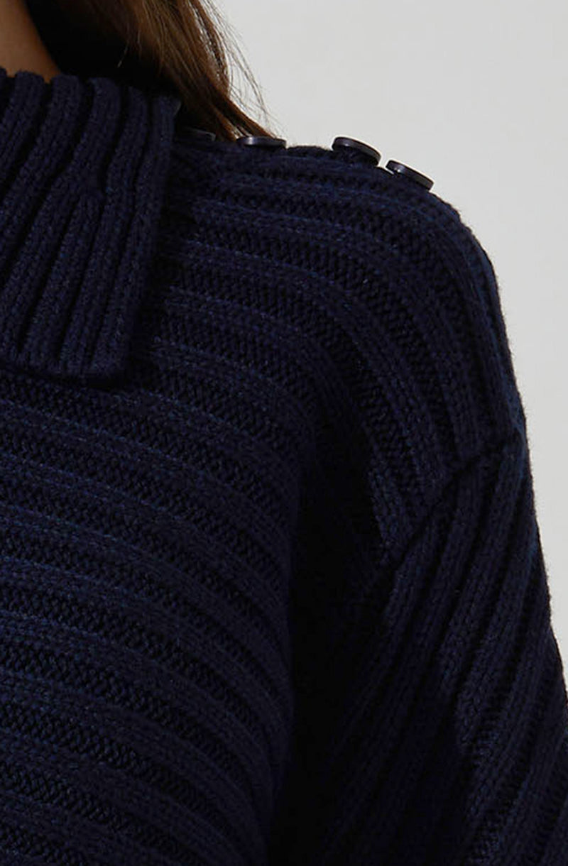 A close-up view of a dark navy blue knitted sweater with a ribbed collar and shoulder detailing featuring three black buttons. The sweater has a textured, chunky knit pattern.