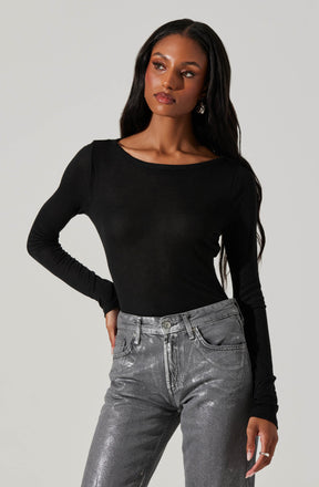A woman is wearing a fitted black long-sleeve top with a rounded neckline and high-waisted metallic silver jeans with a slightly faded appearance.