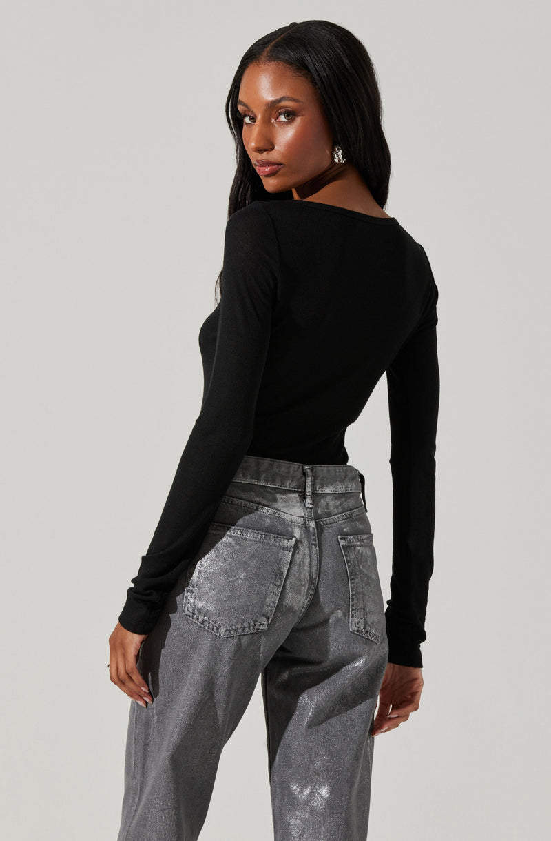 A woman is wearing a fitted, long-sleeve black top with a round neckline and a pair of high-waisted, relaxed-fit gray jeans with a slightly faded wash.