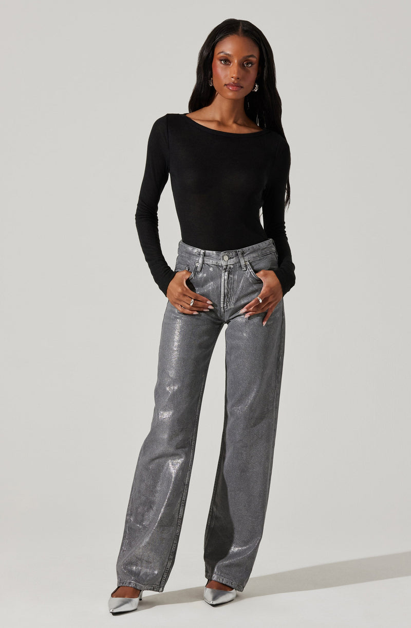A woman is wearing a fitted black long-sleeve top with a round neckline, paired with high-waisted, loose-fitting metallic silver jeans. She is also wearing silver pointed-toe shoes.