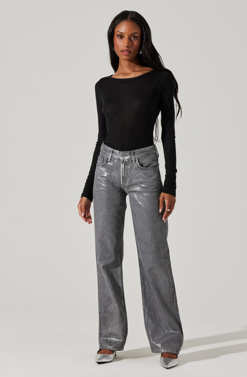 A woman is wearing a fitted black long-sleeve top with a round neckline, paired with high-waisted, wide-leg jeans in a shiny metallic silver color. She completes her outfit with silver pointed-toe shoes.