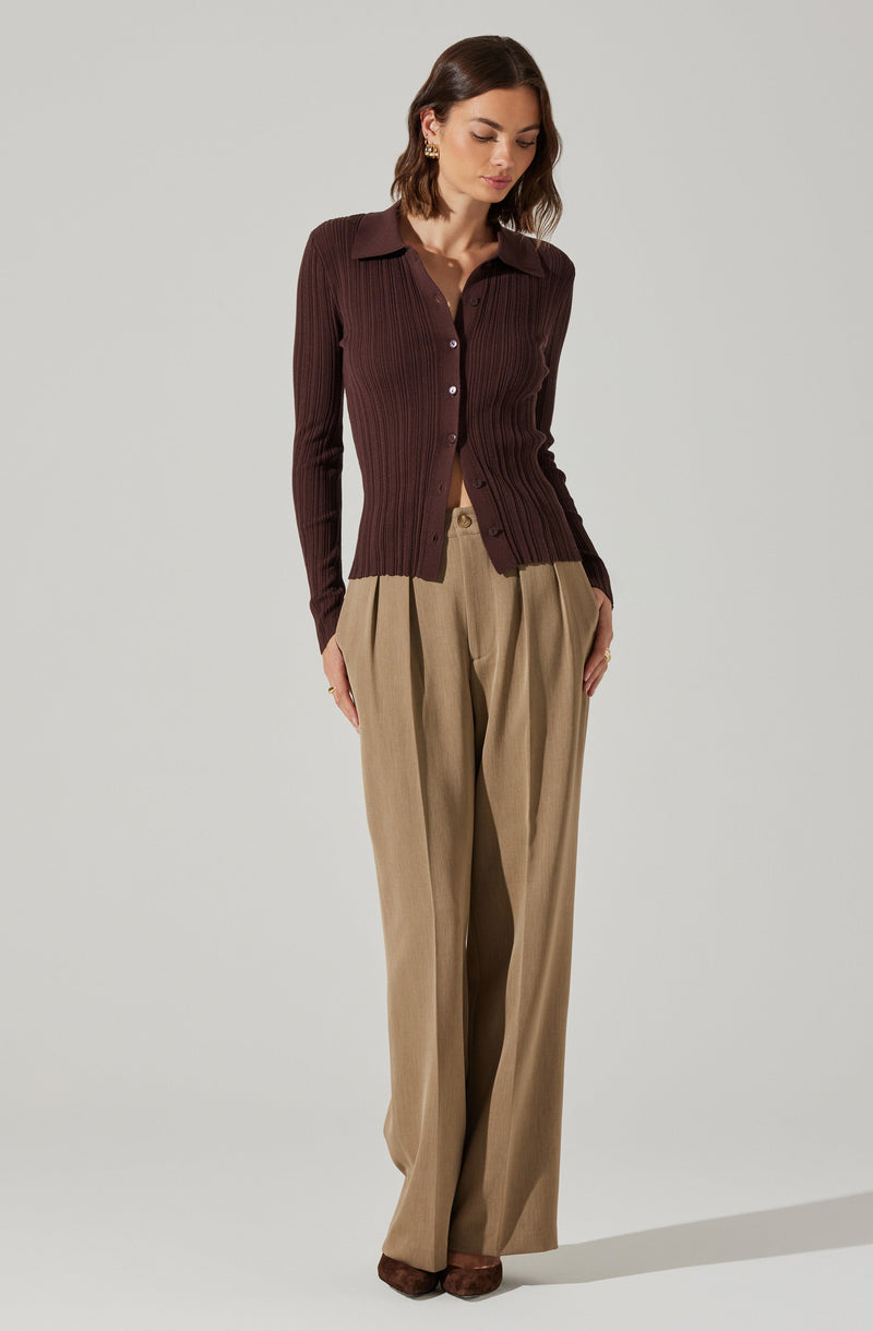 A woman is wearing a fitted, long-sleeved, dark brown ribbed cardigan with a collar and button-down front, paired with high-waisted, wide-leg beige trousers.