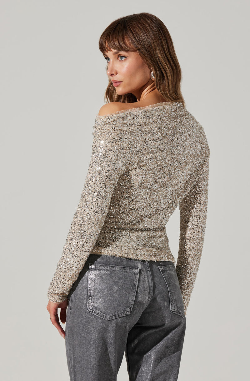 A woman is wearing a long-sleeved, off-the-shoulder top that is entirely covered in sparkling, silver sequins. She paired it with high-waisted, faded black jeans.